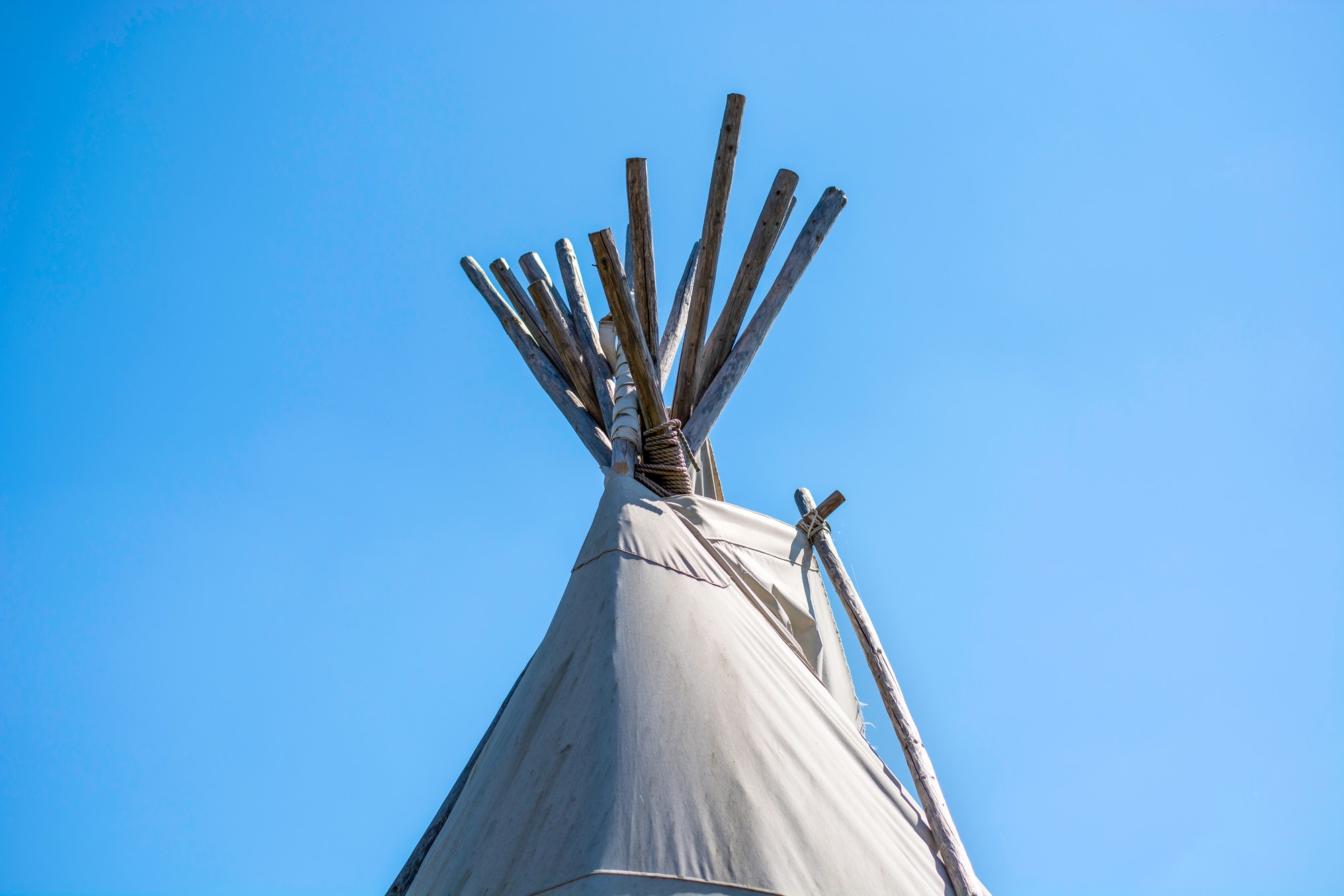Top of a traditional wigwam lodge or teepee tent against clear blue sky background